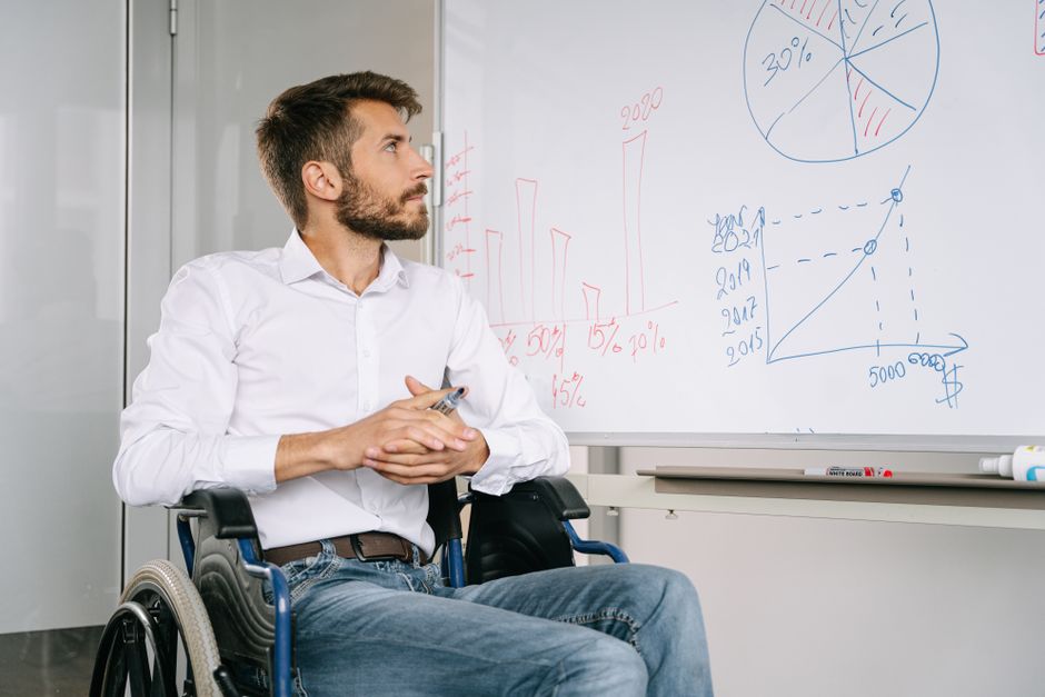 Young man in wheelchair analyzing charts on whiteboard in office setting.